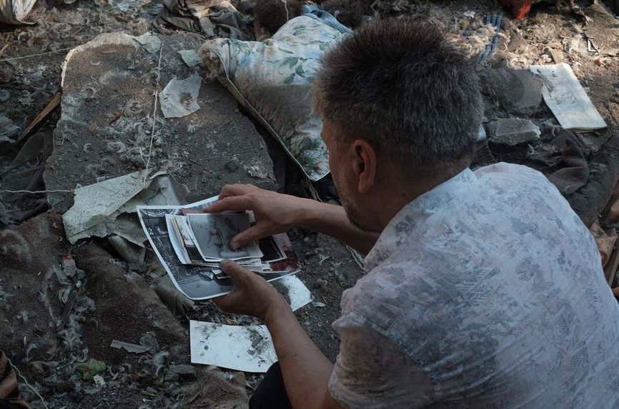 Мужчина собирает фотографии своих родных, разбросанные возле разрушенной пятиэтажки, Николаев